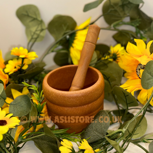 A wooden mortar and pestle hand grinder is displayed with a background of yellow flowers and green leaves.