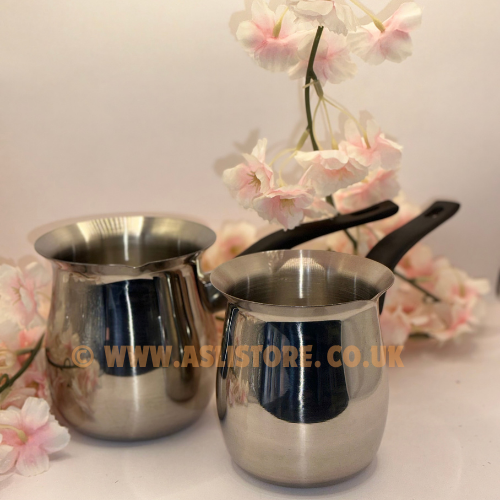 Two metal coffee stirring cups with handles, placed on a surface with pink flowers in the background.