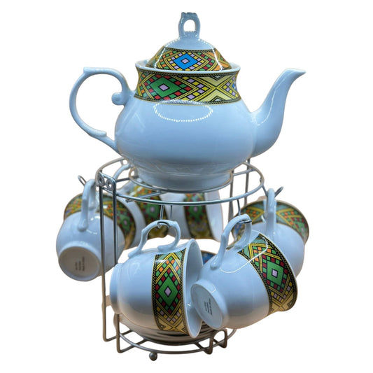 A ceramic Habesha tea pot set with matching cups, each with hand-painted designs, displayed on a metal stand.