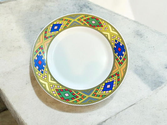 A traditional Habesha porcelain serving plate with a colorful geometric pattern around the border on a white background.