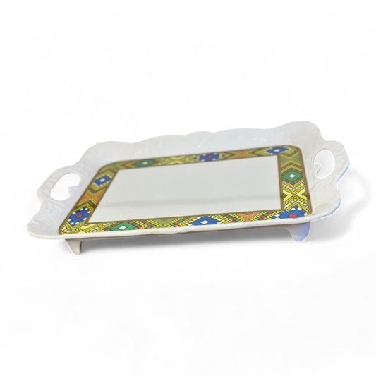 A traditional Ethiopian serving plate with a geometric Tilet Zuria design, made of white plastic with colorful patterns along the edges.